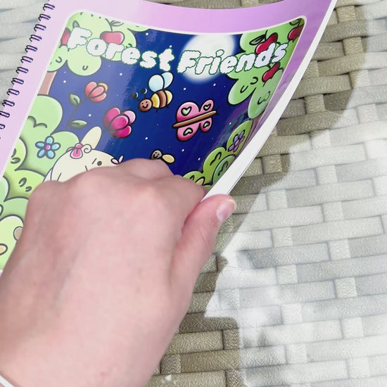 Forest Friends: Premium Wire-Bound Woodland Colouring Book held above a glass table with colorful woodland designs.