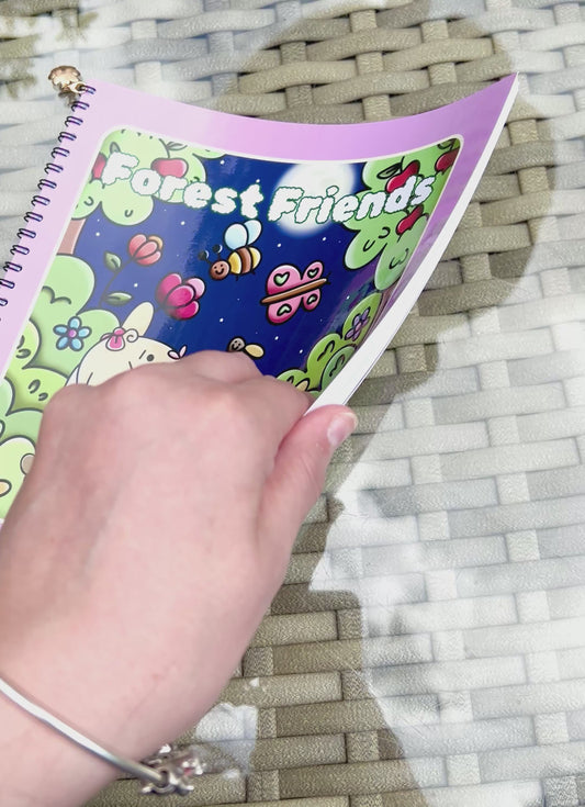 Forest Friends: Premium Wire-Bound Woodland Colouring Book held above a glass table with colorful woodland designs.